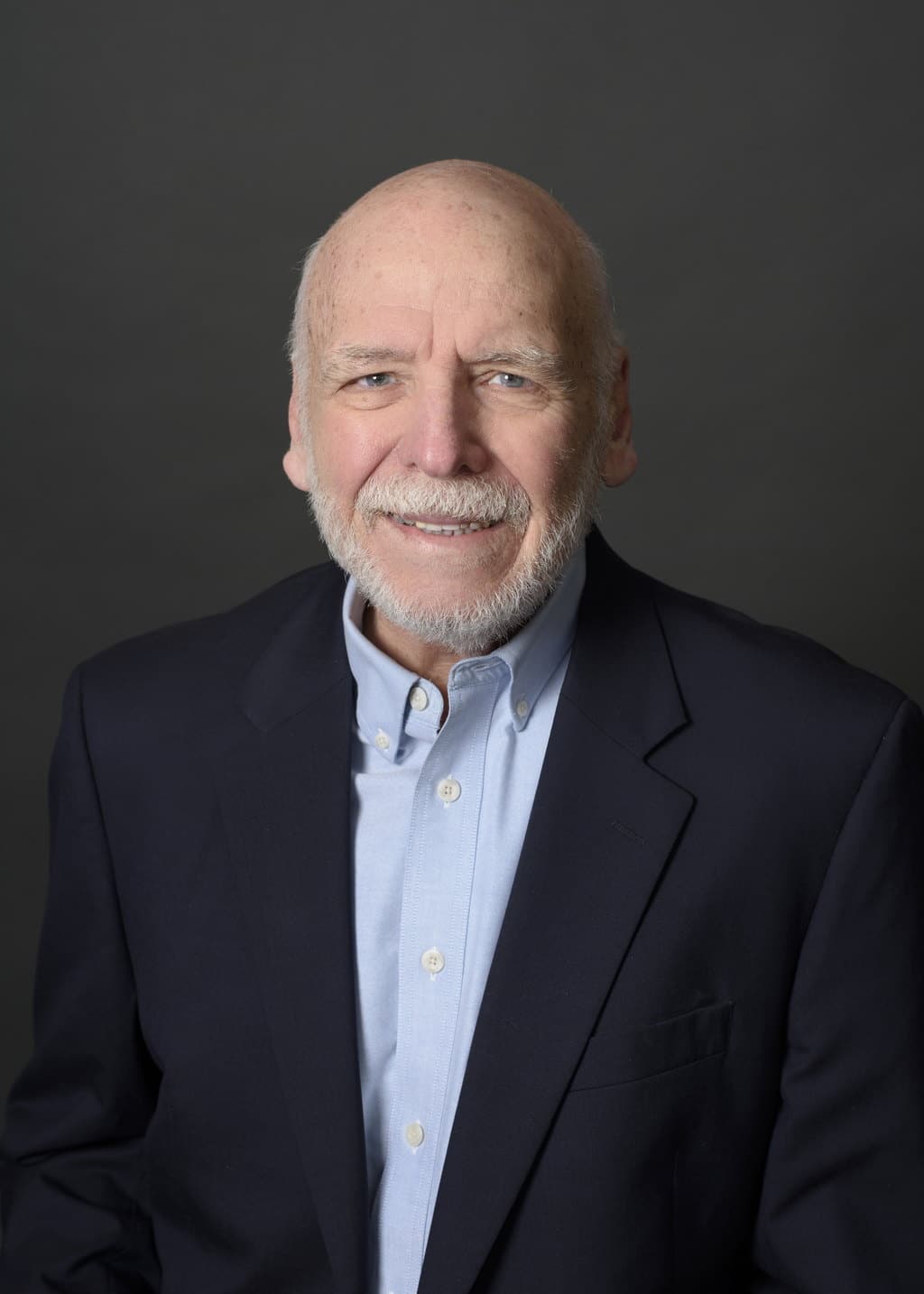 Dick Walrath, Associate Broker at State Wide Real Estate of Houghton, wearing a navy blazer over a light blue shirt against a gray studio backdrop.