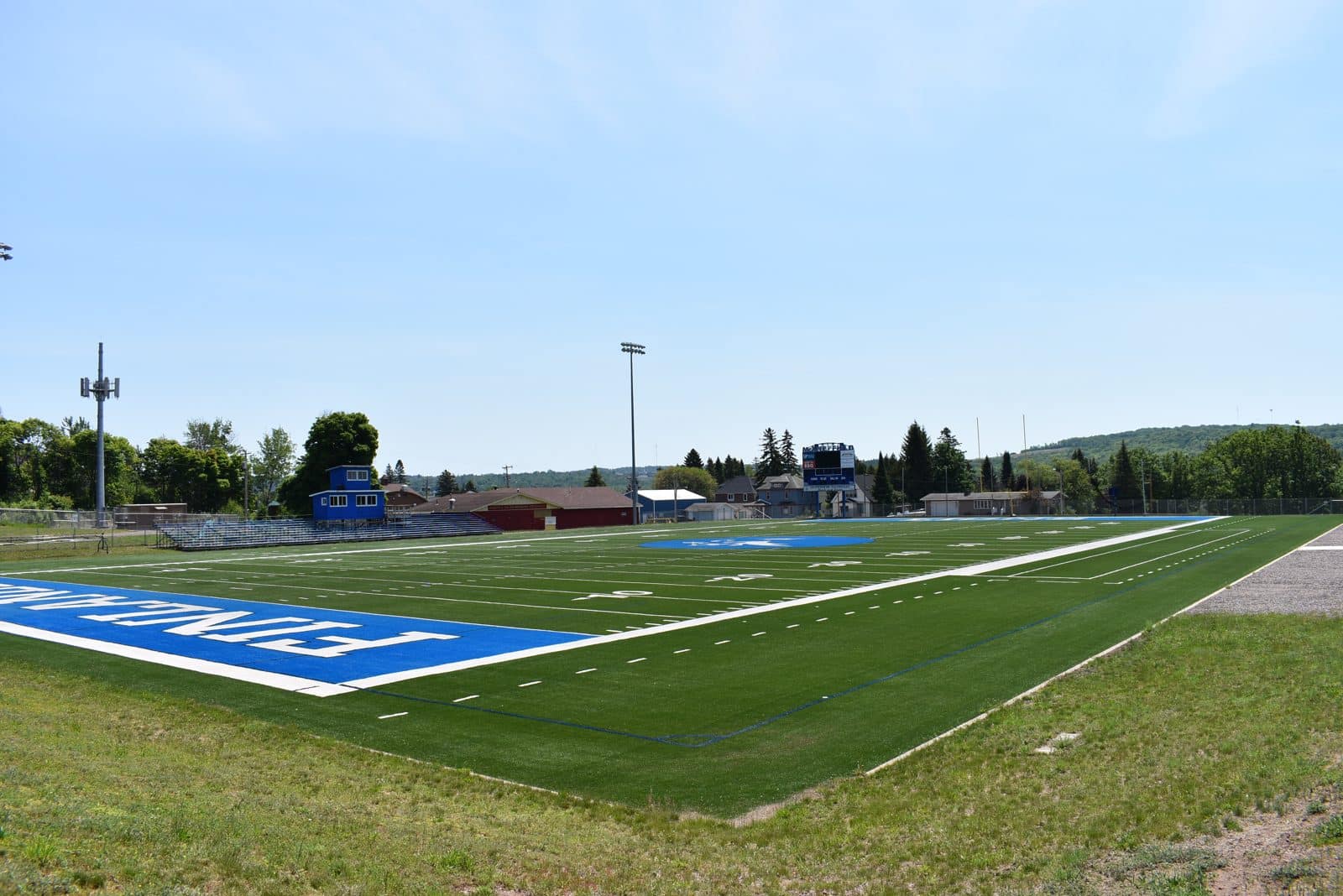 School athletic field, Hancock MI | State Wide Real Estate of Houghton High school football field with bleachers and press box below wooded hills in Hancock, Michigan