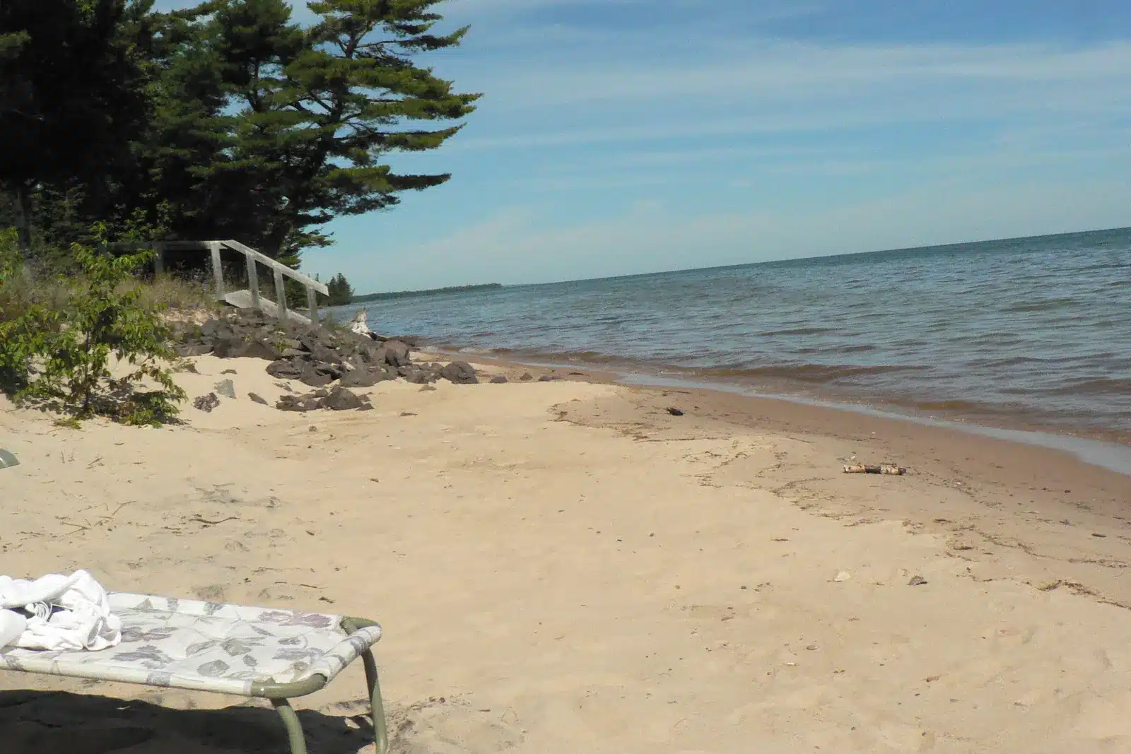 Wooden stairs leading down to a sandy Lake Superior beach with a lounge chair near the water.