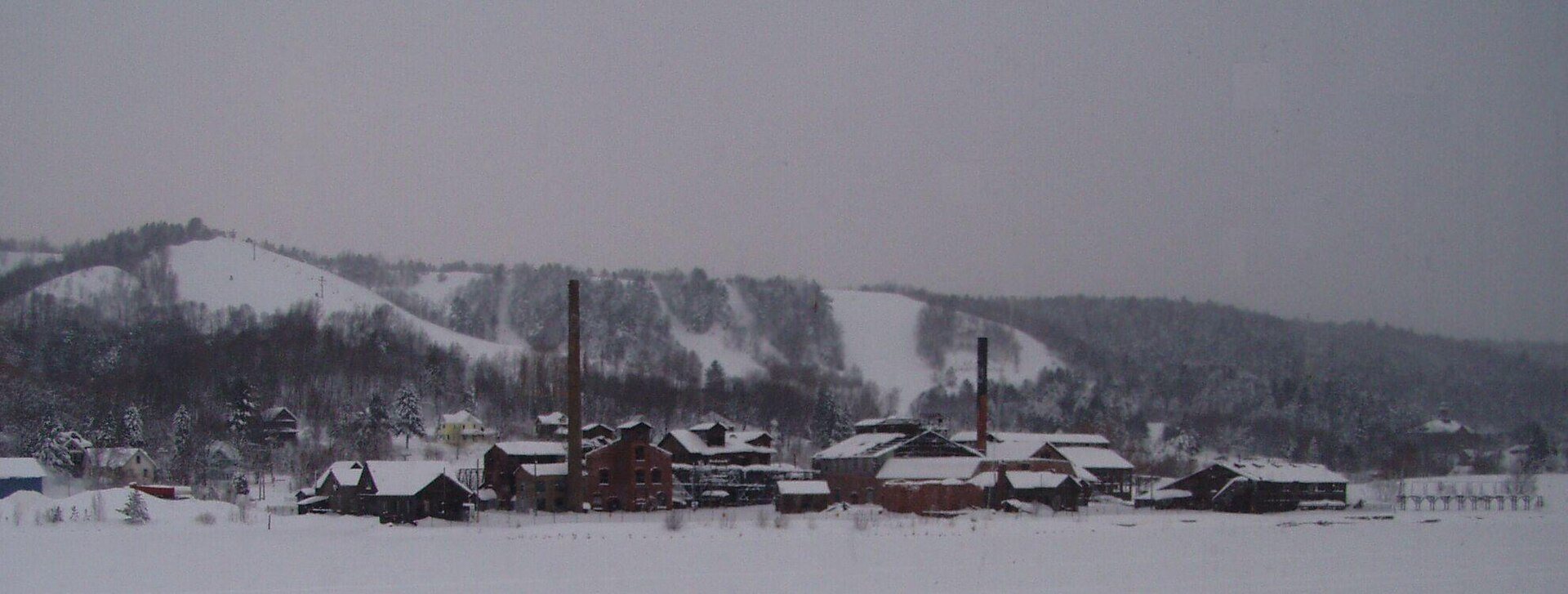 Quincy Smelter in winter, Hancock MI | State Wide Real Estate of Houghton Snow-covered Quincy Smelter buildings on the frozen Portage Canal shore in Hancock, with ski runs cut into the hillside behind