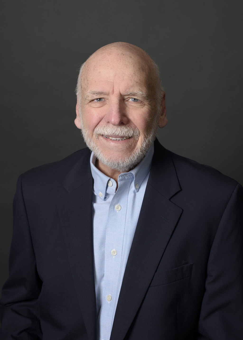 Dick Walrath, Associate Broker at State Wide Real Estate of Houghton, wearing a navy blazer over a light blue shirt against a gray studio backdrop.