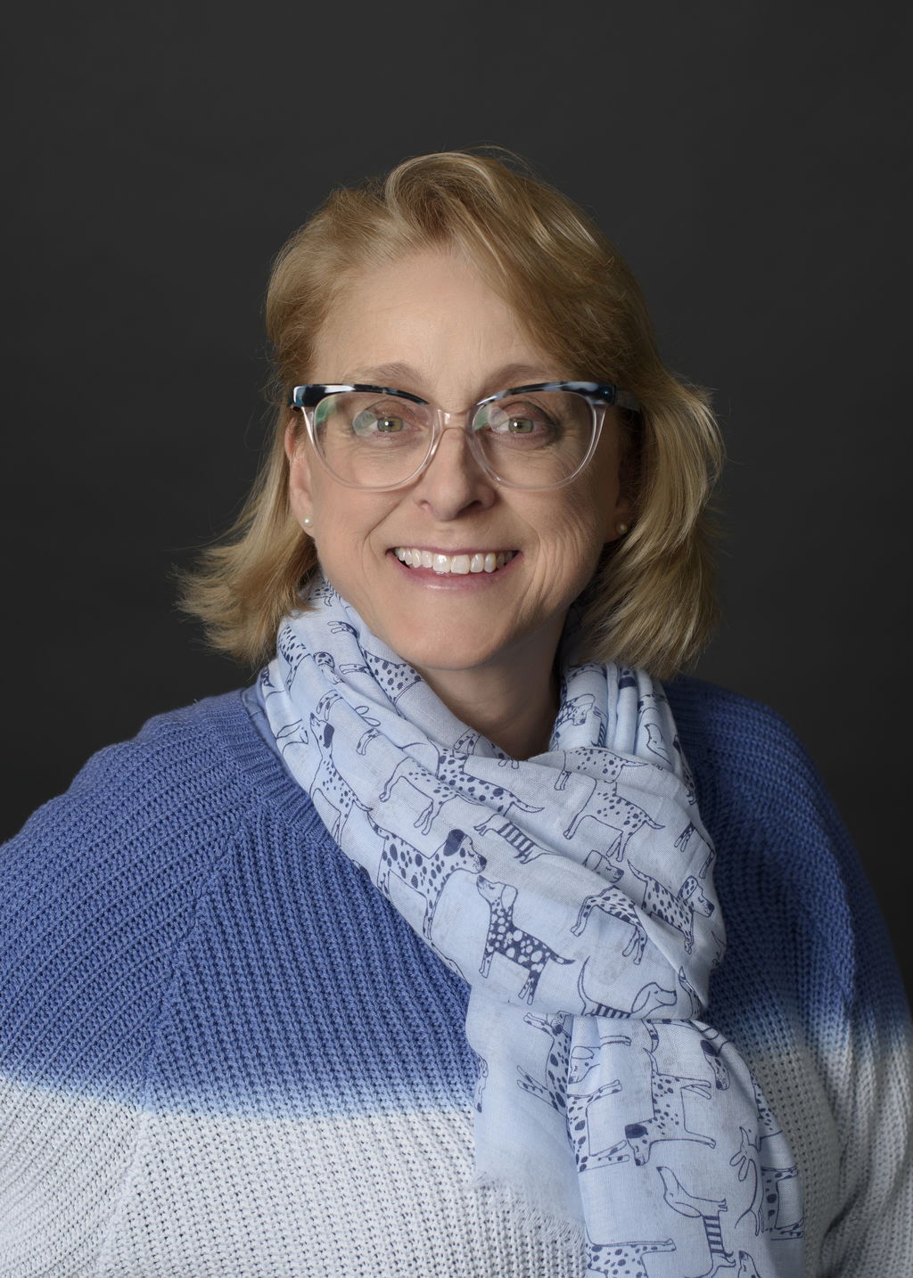 Kathy Liimatta, Co-Owner of State Wide Real Estate of Houghton, wearing a blue and white sweater with a patterned scarf against a gray studio backdrop.